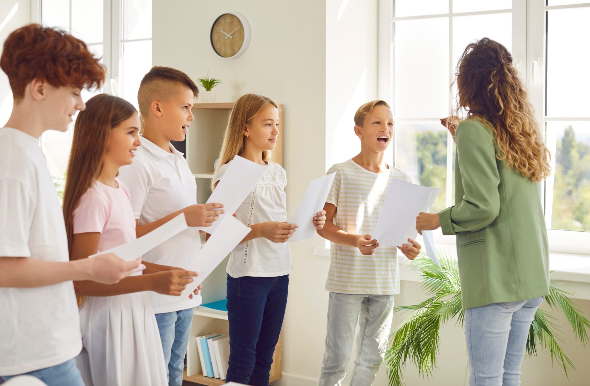 Young school children standing in a circle with their young female teacher having music lesson