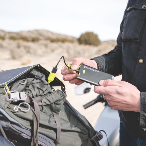 אדם משתמש בחבילת סוללות SHERPA15 של חברת סוללת גיבוי בהספק 15Wh עם כבלי L+M כדי להתחבר לתחנת כוח סולארית המשולבת בתיק גב, ומציג טכנולוגיה פוטו-וולטאית ניידת וייצור אנרגיה מתחדשת בסביבה חיצונית.