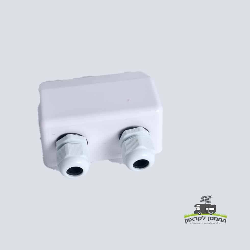 קופסת חיבורים פוטו-וולטאית לבנה מפלסטיק עם שתי בלוטות כבלים בצד אחד, מיועדת להתקנות אנרגיה סולארית מאובטחות על הגג וניהול יעיל של כבלי חשמל במערכות אנרגיה מתחדשת; רכיב אידיאלי עבור פאנלים סולאריים פוטו-וולטאיים, תשתית לייצור חשמל ואחסון אנרגיה (אגירה סולרית), מוצגת על רקע בהיר חלק.