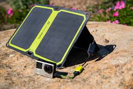 פאנל סולארי מתקפל NOMAD 14 בהספק 14W, עם חיבור USB (5.1-15V), ומצלמת אקשן מוצבים על סלע בשטח, מחוברים בכבל טעינה—מציגים שימוש בטכנולוגית פוטו-וולטאית לייצור חשמל מאנרגיית שמש ומתאימה לחנות כוח ניידות או מערכת אגירה מתקדמת באנרגיה מתחדשת בהרפתקאות וסביבות מחוץ לרשת.
