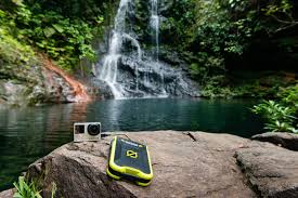 מצלמת אקשן קומפקטית וסוללת גיבוי עמידה מדגם VENTURE30 IPX6 28Wh בעלת שוליים צהובים - שתוכננה לשימוש באנרגיה מתחדשת עם יכולת טעינה סולארית וטכנולוגיה פוטו-וולטאית מתקדמת - ממוקמות על סלע ליד מפל יער ובריכה צלולה, וממחישות ייצור אנרגיה סולארית מחוץ לרשת החשמל בטבע.