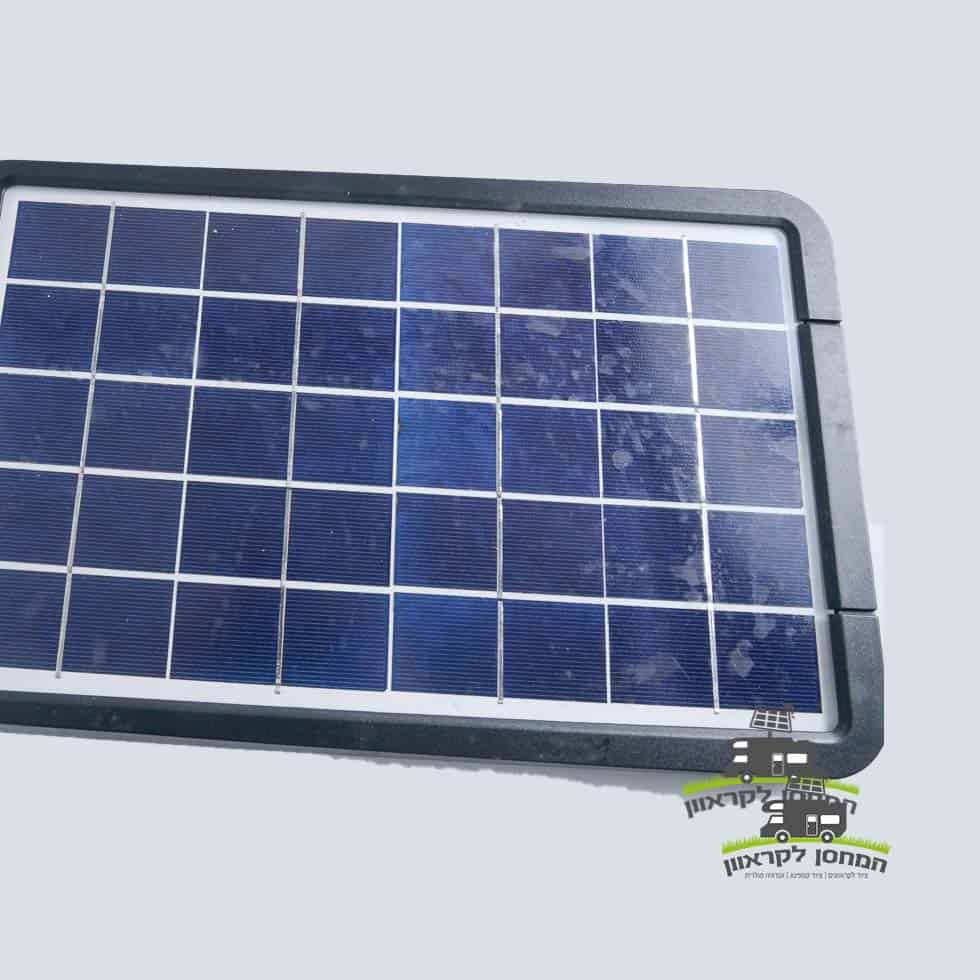 תקריב של פנס LED סולארי 15W 6000LM מלבני (פרוז'קטור לד סולארי) עם מסגרת שחורה, הכולל פאנלים פוטו-וולטאיים מתקדמים לייצור חשמל באנרגיה מתחדשת, על רקע בהיר; ציוד ידידותי לסביבה אידיאלי עבור קרוואנים (מוצרים לקרוואנים) או ציוד מחנאות (ציוד לקמפינג). לוגו קטן עם טקסט בעברית מופיע בפינה הימנית התחתונה, המדגיש פתרונות אנרגיה סולארית ברי קיימא ומחוץ לרשת.