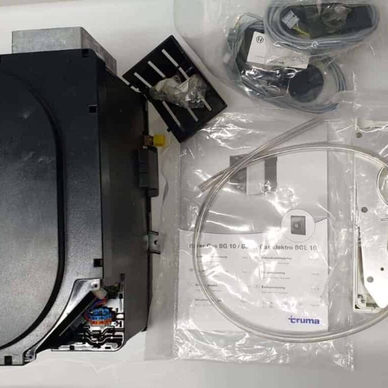 דוד מים לגז וחשמל (TRUMA) עם תווית, חיווט, צינורות, אביזרי התקנה, מדריכים ורכיבי ציוד מחנאות נוספים המוצגים על משטח לבן - אידיאלי לשילוב עם מערכות אנרגיה סולארית, מערכי טכנולוגיה פוטו-וולטאית, פתרונות לייצור חשמל ותשתית אנרגיה מתחדשת.