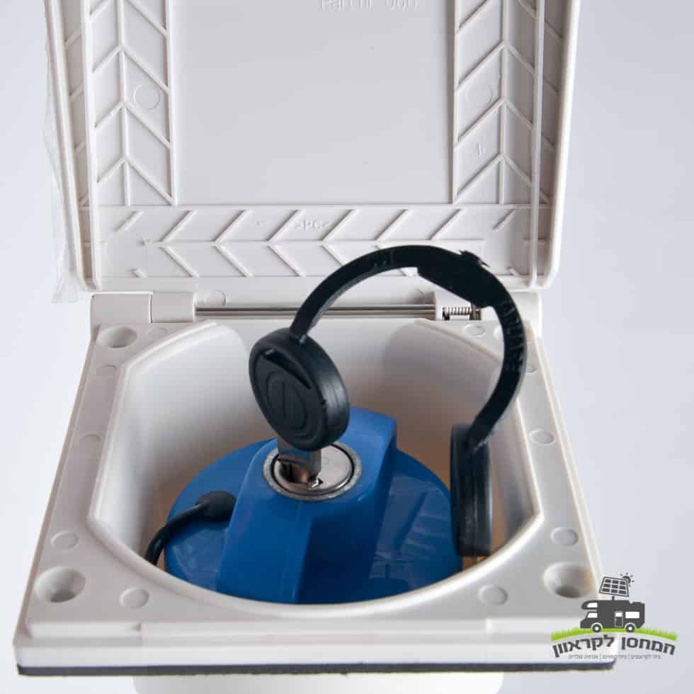 תקריב של מכסה מילוי מים כחול הניתן לנעילה עם מפתח, המשובץ במארז פלסטיק לבן ועמיד - עיצוב פתוח חלקית לגישה מאובטחת בתחנות כוח סולאריות פוטו-וולטאיות. רכיב חיוני לתחזוקת תשתית אנרגיה סולארית; כולל לוגו המקושר לאנרגיה מתחדשת וייצור חשמל בר-קיימא, גלוי בתחתית ימין.