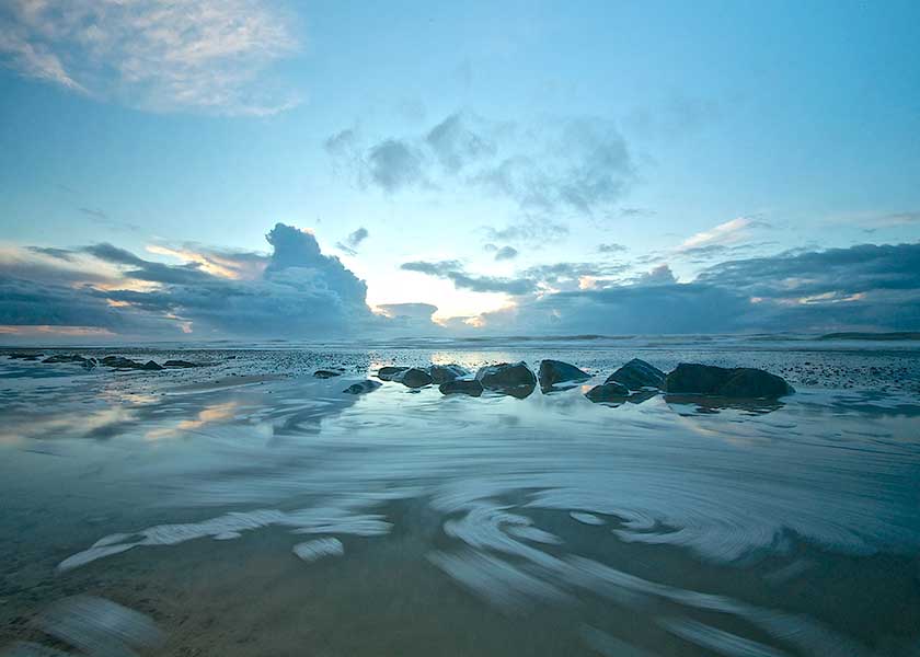 Stille aften, solen gemmer sig på himlen bag de blågrå skyer inden den går i havet, vand og bølger tegner drømmeagtige billede i vandkanten