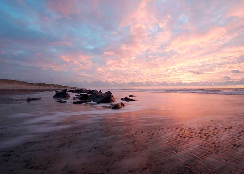 Tidlig morgen ved stranden himlen står i en flot blanding mellem blå, rød og orange nuancer hvor lyset blødgøres af de flotte skyformationer