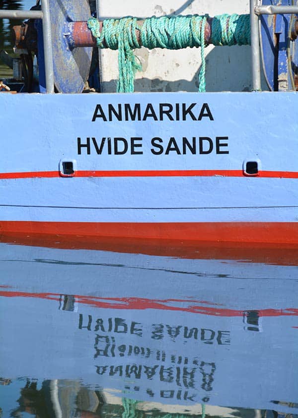 En af de flotte blå kuttere i havnen i Hvide Sande spejler sig smukt i det spejlblanke vand