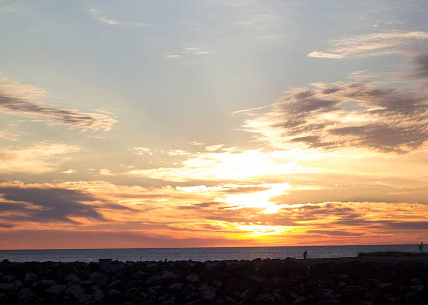Solnedgang over nordmolen i Hvide Sande - folk går en sen aftentur og nyder at solen går i havet