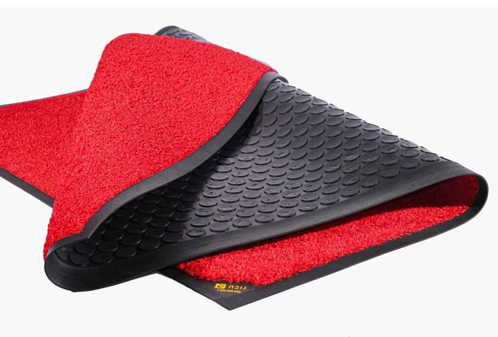 שטיח אדום נגד החלקה עם משטח מחוספס ובסיס גומי שחור המונע החלקה, מקופל חלקית כדי להראות את שני הצדדים. אידיאלי כשטיח ממותג לעסק או כתוספת מסוגננת לכל כניסה.