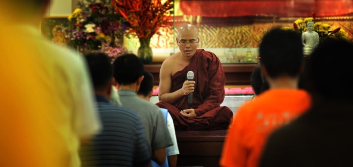 Picture of a monk in the background holding a mic coaching and discussing life with onlookers. This is the category picture for the spiritual life coach category on No Relent TV.