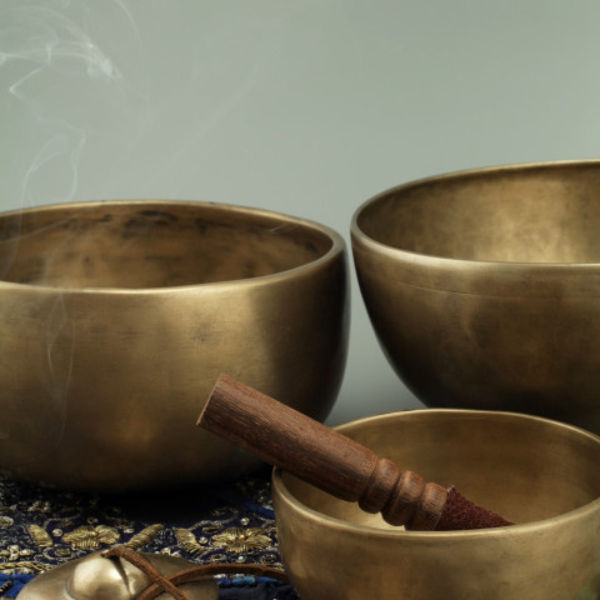 Three brass singing bowls on a blue cloth.