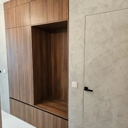 Ugrađeni drveni ormar sa sjedećom nišom uz dekorativni zid prekriven sivom žbukom.