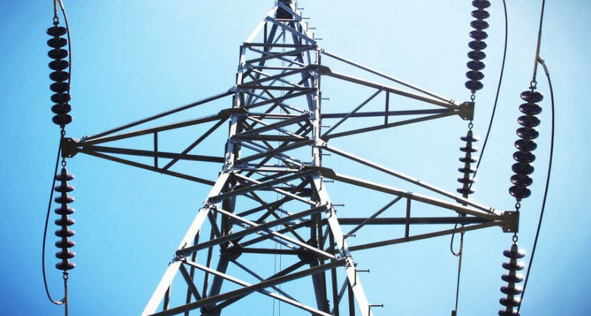 A close-up view of an electrical transmission tower with power lines and insulators against a clear blue sky.