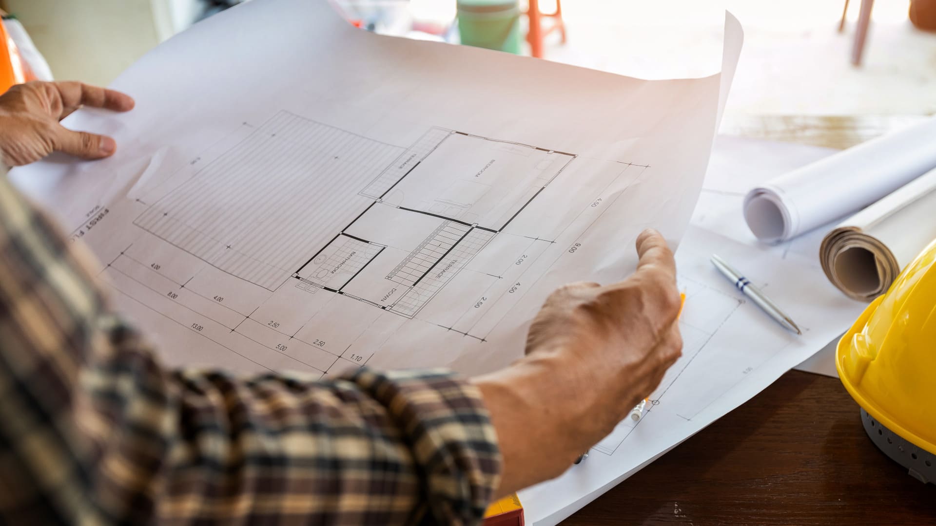 A man is holding blueprints and a hard hat.