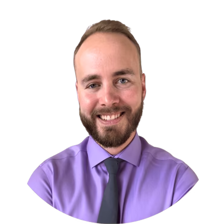 A man with a beard and short hair smiles at the camera, wearing a light purple shirt and a dark tie on a white background.