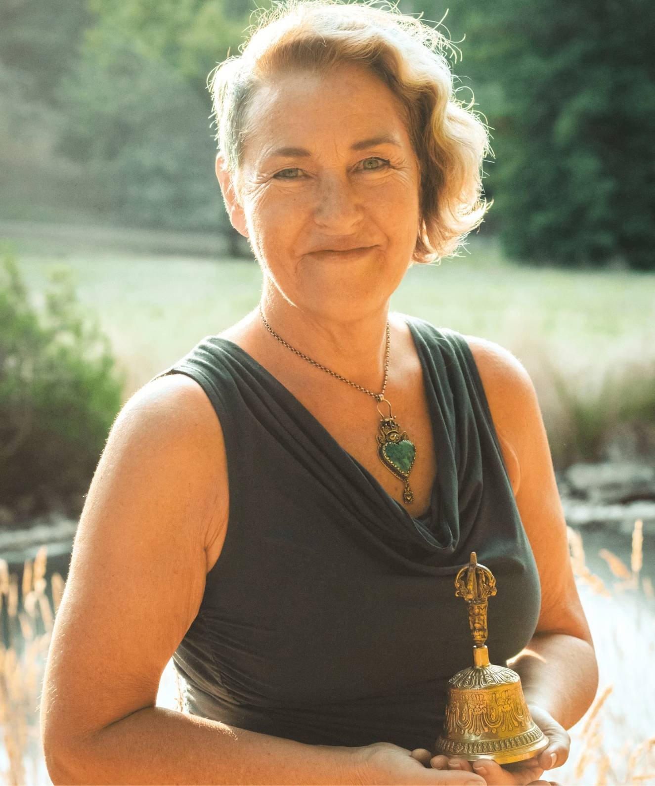 maggie-ostara-sovreignity-by-design Maggie Ostara smiling outdoors holding a golden ritual bell, representing Sovereignty by Design Human Design teachings.