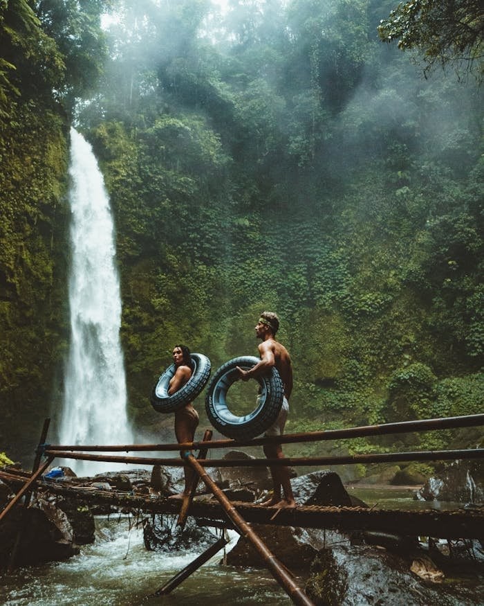 A couple in swimwear with float tubes exploring a lush waterfall in Bali, Indonesia.