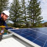 Solar panel technician with drill installing solar panels on roof
