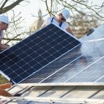 Male workers installing solar photovoltaic panel system. Electricians mounting blue solar module on roof of modern house. Alternative renewable energy ecological concept.