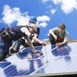 Workers installing alternative energy photovoltaic solar panels on roof