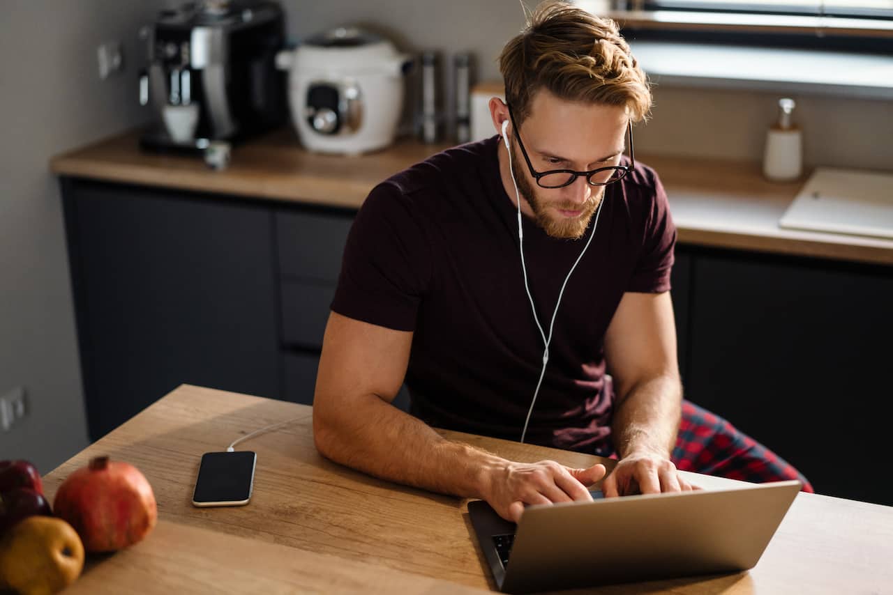A man in pajamas working remotely from the kitchen with his laptop.