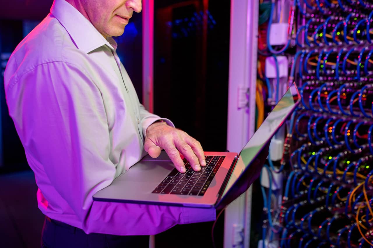A man utilizing network infrastructure using a laptop in a server room.