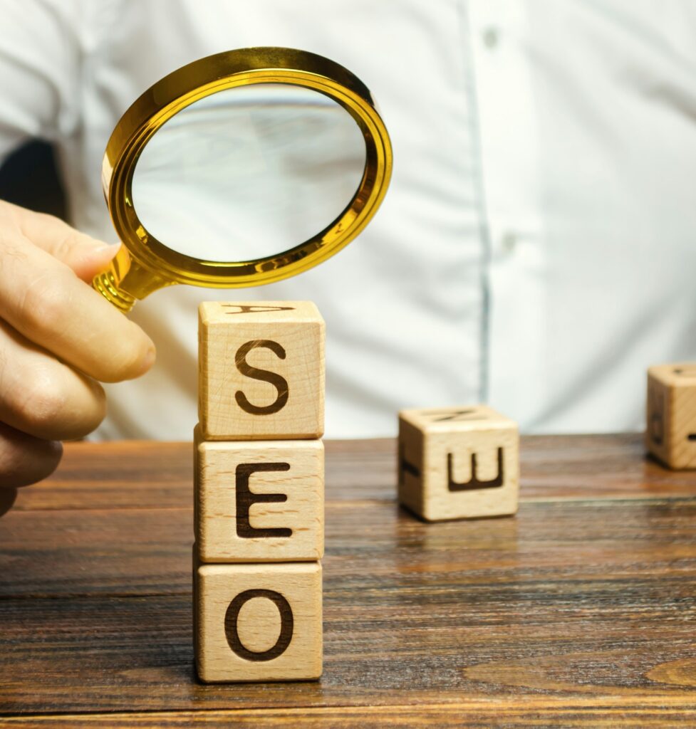 Person holding a magnifying glass over wooden blocks spelling out SEO, representing SEO services in Denver.