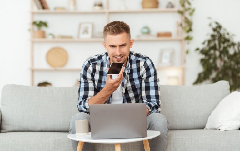 Man using voice search on smartphone while working on laptop – voice search SEO optimization