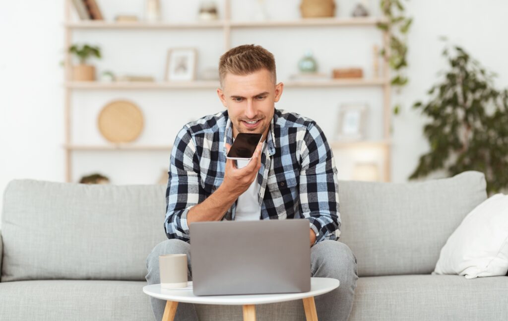 Man using voice search on smartphone while working on laptop – voice search SEO optimization