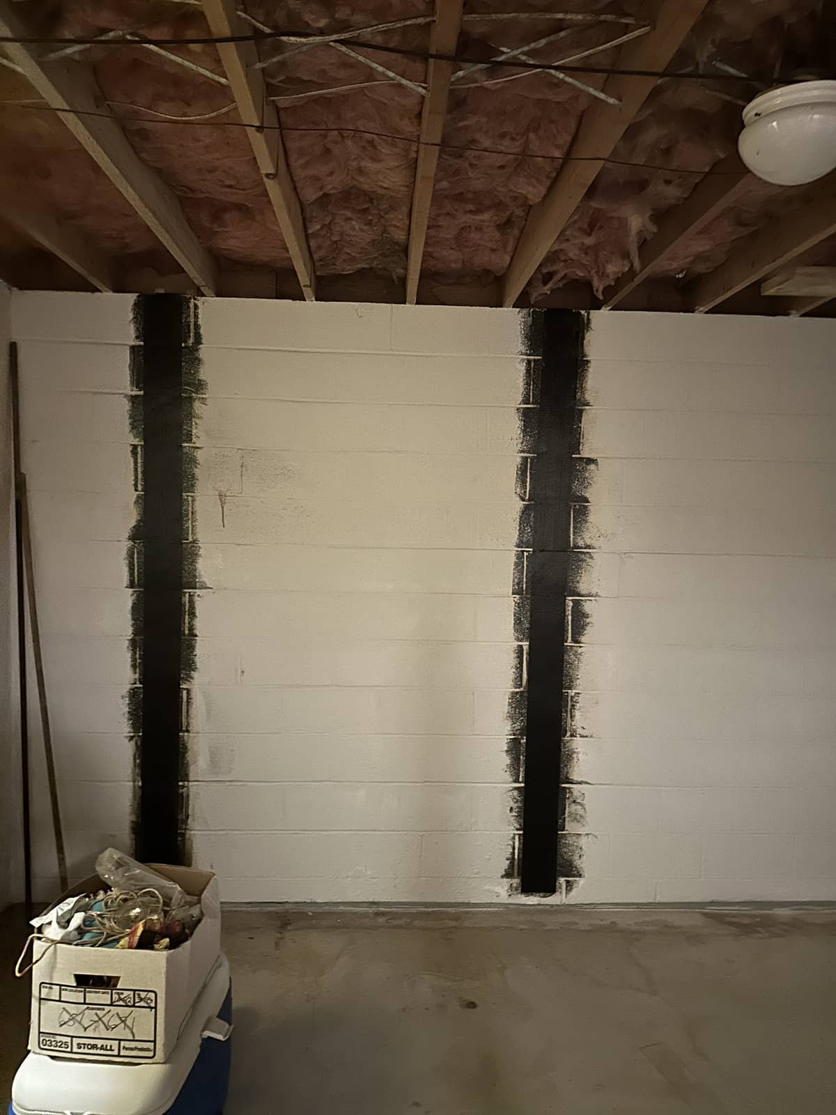 Basement wall with exposed ceiling insulation and two vertical black strips painted on the white concrete blocks; a box of tools is on the floor in the corner.
