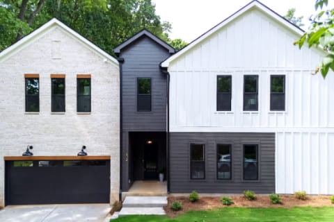 Modern two-story house with a combination of white brick and black siding, featuring a two-car garage and landscaped front yard.
