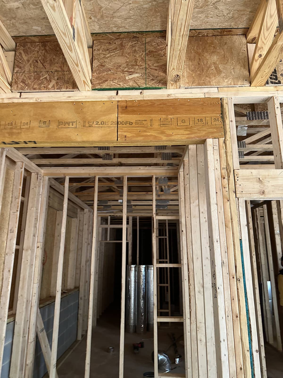 Wood framing of a house under construction, showing exposed beams, joists, studs, and ductwork in an unfinished interior.