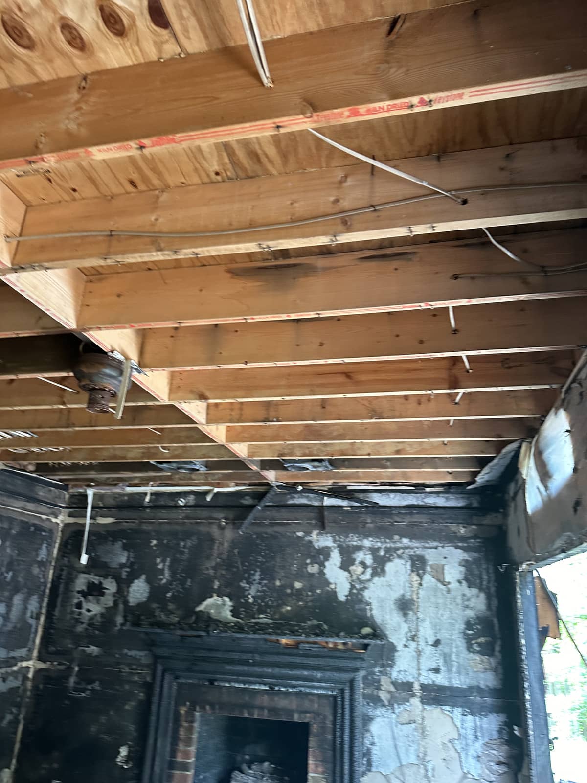 Exposed wooden ceiling beams and wiring in a room with smoke-damaged, charred walls and a fireplace.