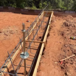 Rebar and wooden forms set up for a concrete foundation on a construction site with dirt ground and tools scattered nearby.