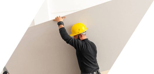 Worker in a hard hat measuring a wall with a tape measure.