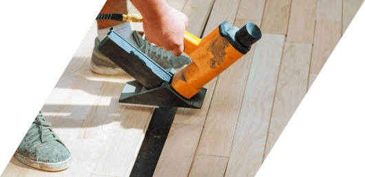 Person using a caulking gun on a floor next to a metal threshold.