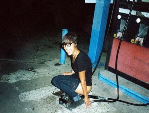 A woman kneeling down next to a gas pump, sporting an