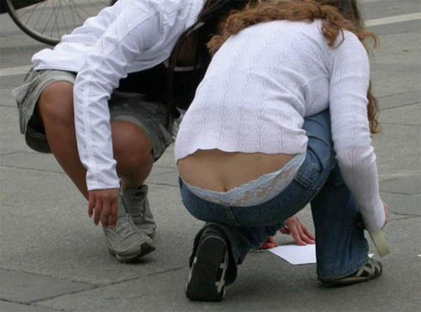 Two women crouching down on the ground, with a whale tail in their hands.