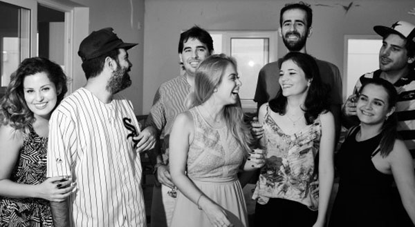 A black and white photo capturing a group of people engrossed in Weekend Confessions in a cozy living room.