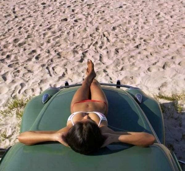A bikini-clad babe lounging on a vibrant green car.