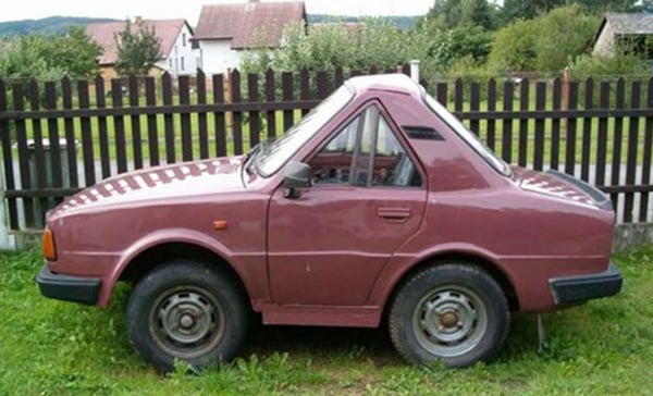 A cool pink car parked next to a grassy fence.