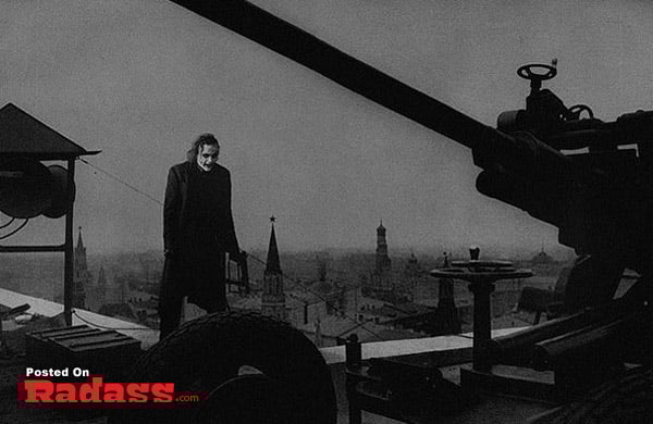 A man with superpowers posing next to a cannon in a city.