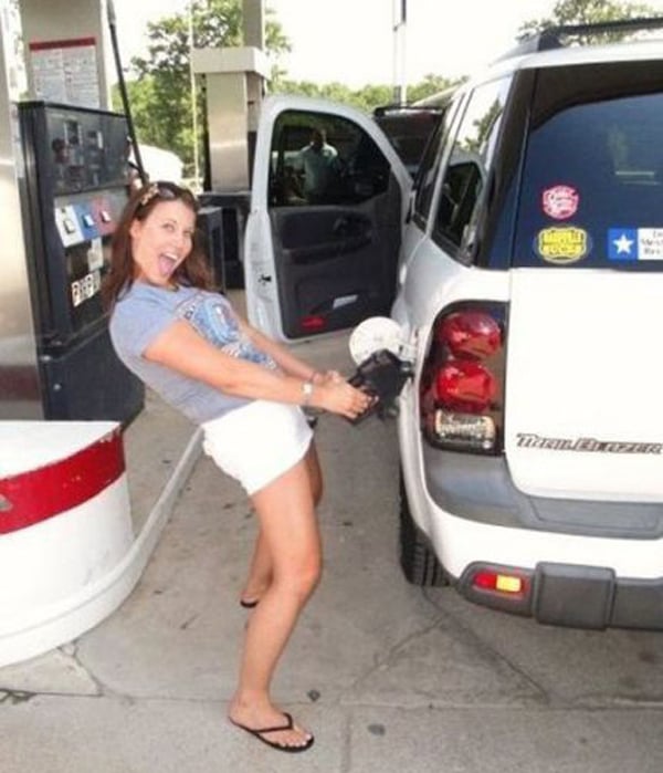 A woman filling up her car at a gas station, pondering