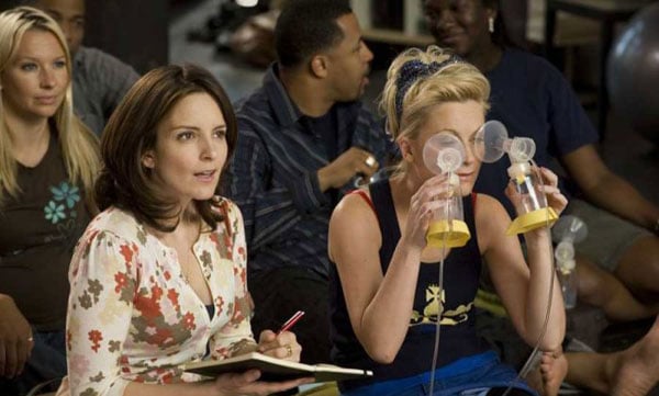 A group of women are sitting in a room holding cell phones, engaging in conversations with one another while occasionally glancing at their screens.