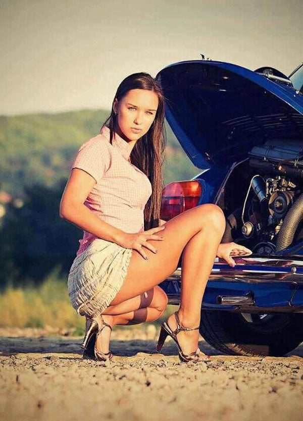 A babe crouching down next to a blue car.