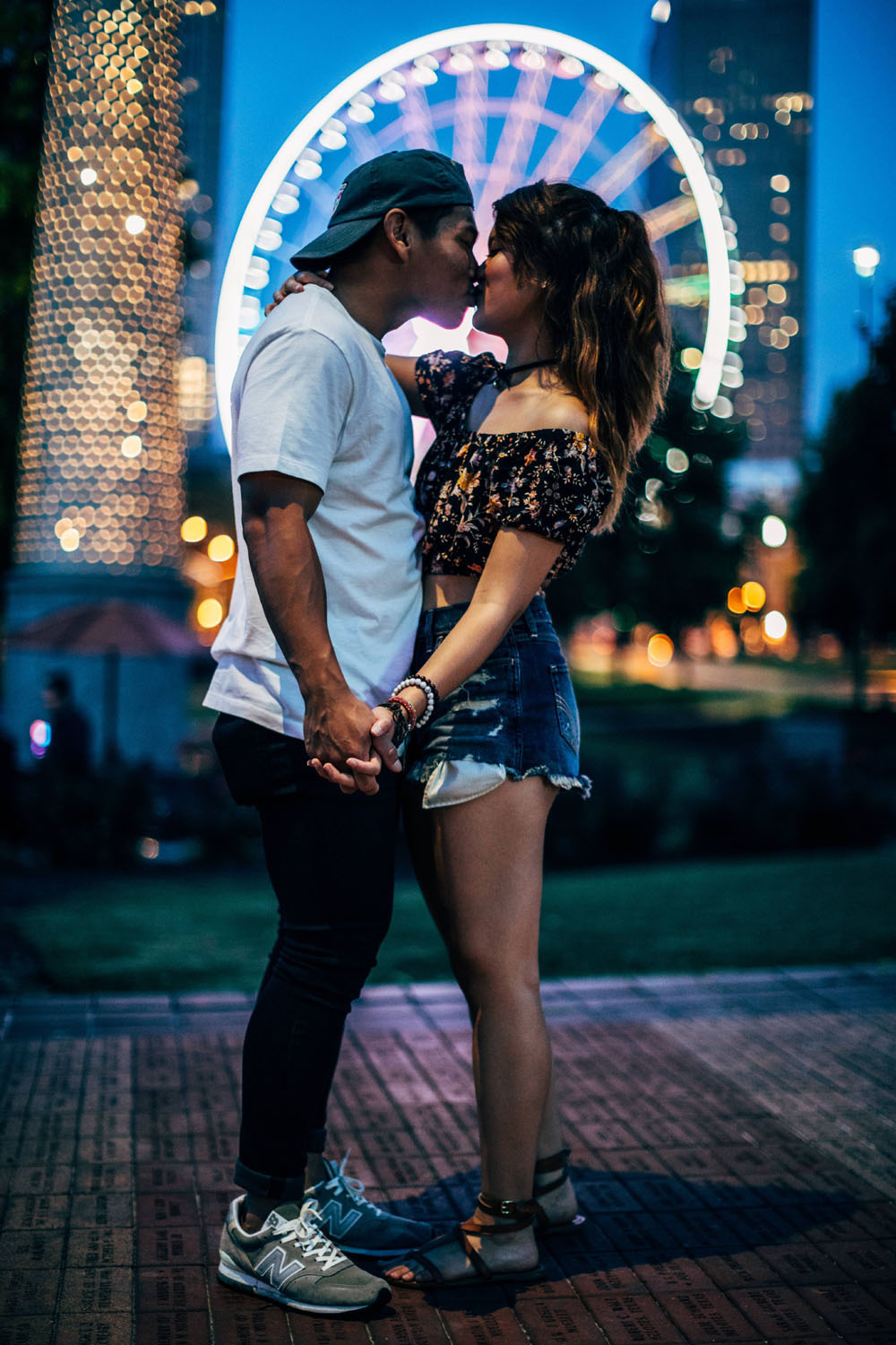 A couple sharing a tender kiss in front of a majestic ferris wheel on a Saturday morning, capturing cool pics of their love and happiness.