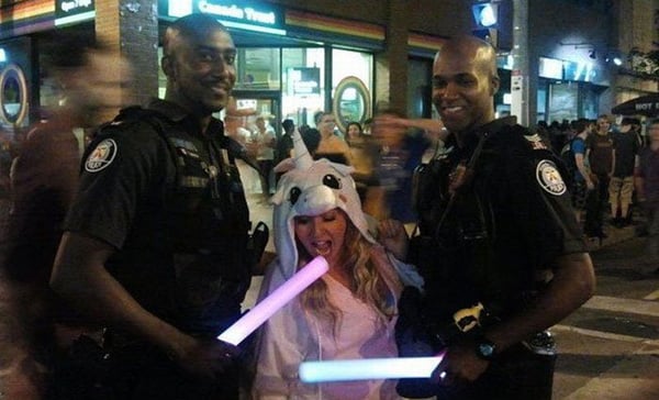 Two police officers pose with lightsabers in front of a crowd, creating an