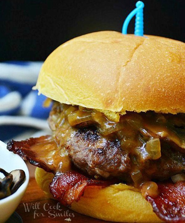 An awesome burger with bacon and onions artfully presented on a wooden board.