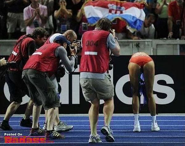A woman in a red bikini is being photographed by a crowd.