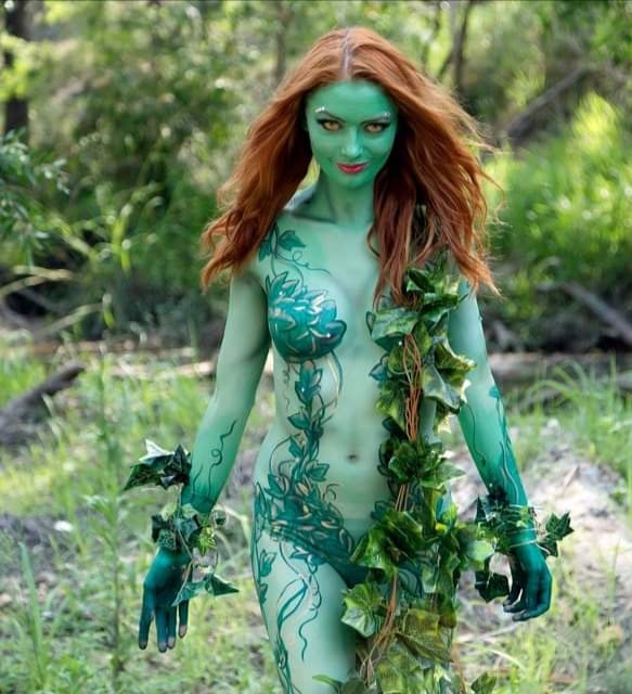 A woman adorned in vivid green body paint emerges among the trees like one of the enchanting Painted Ladies.